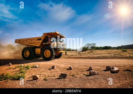 Ein riesiger gelber Bergbaulaster auf einer unbefestigten Straße mit einer Staubspur Stockfoto