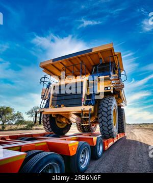 Schwertransporter riesiger gelber Bergbaulaster oben auf einem Anhänger auf einer unbefestigten Straße Stockfoto