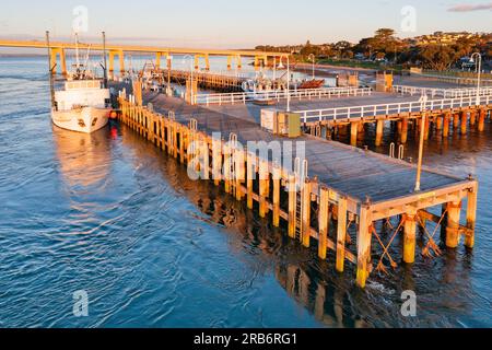 Ein Fischerboot, das an einem hölzernen Anleger im Morgensonnenschein in San Remo auf Phillip Island in Victoria, Australien, festgemacht hat. Stockfoto