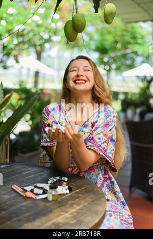 Porträt einer wunderschönen blonden Künstlerin und Illustratorin, die am Tisch sitzt und ihre Acrylfarben in der Hand hält Stockfoto