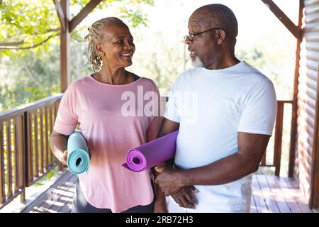 Portrait eines glücklichen älteren afroamerikanischen Ehepaars, das Yoga-Matten auf der Terrasse hält. Seniorenleben, Entspannung, Ruhestand, gesundes Leben, Fitness, Stockfoto