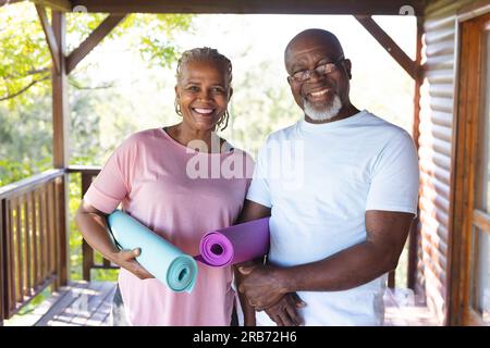 Portrait eines glücklichen älteren afroamerikanischen Ehepaars, das Yoga-Matten auf der Terrasse hält. Seniorenleben, Entspannung, Ruhestand, gesundes Leben, Fitness, Stockfoto