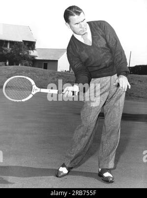 New Jersey: ca. 1953 Ein Mann, der mit einer anderen Sportausrüstung posiert und Ähnlichkeiten mit der Körperhaltung zeigt. Hier benutzt er einen Tennisschläger. Stockfoto