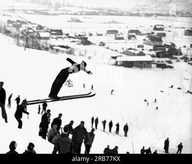 Vereinigte Staaten: c. 1957. Ein Skifahrer startet in die Luft und zeigt in dieser Winterszene großartige Form. Stockfoto