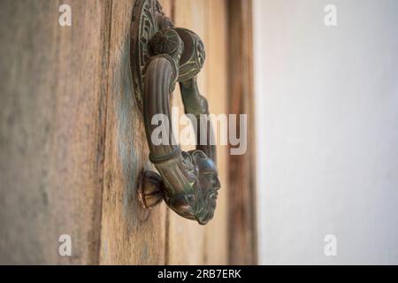 Nahaufnahme eines großen metallischen, bronzefarbenen, kreisförmigen Klopfers einer alten Holztür Stockfoto