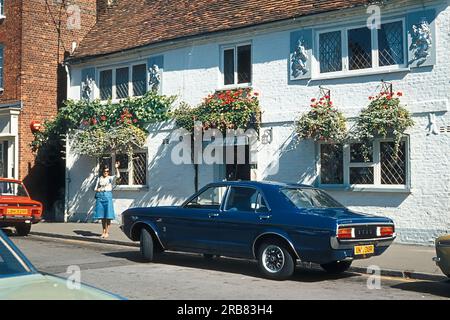 Eine Frau, die neben einem alten englischen Cottage steht, mit einem Ford Granada Auto, das davor geparkt ist. Stockfoto