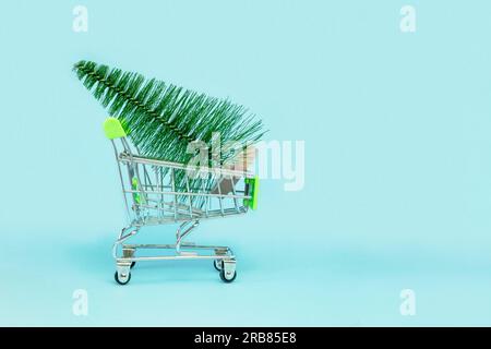 Ein kleiner Weihnachtsbaum ist in einem Einkaufswagen. Künstliche Mini-Weihnachtsbäume in einem Supermarkt-Trolley auf blauem Hintergrund. Weihnachten, Neujahr, Feiertage Stockfoto