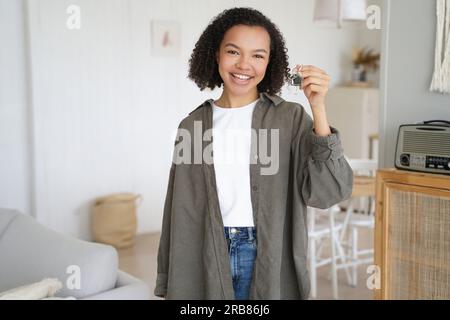 Glückliches Mädchen zeigt Schlüssel zur ersten Wohnung. Ein lächelnder Teenager hat den Hausschlüssel, steht in einem neuen Zuhause. Immobilienvermietungsservice gibt Auslagerung an. Stockfoto