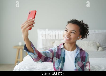 Birassische Teenager-Blogger chatten online per Telefon-Videoanruf und nutzen zu Hause moderne Apps. Lächelndes Mädchen macht Selfie mit Smartphone. Stockfoto