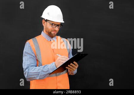 Männlicher Ingenieur in einem weißen Schutzhelm und Orange West. Attraktiver selbstbewusster Bauarbeiter isoliert auf schwarzem Hintergrund. Bereich Kopieren. Er arbeitet in einem Heavy Stockfoto