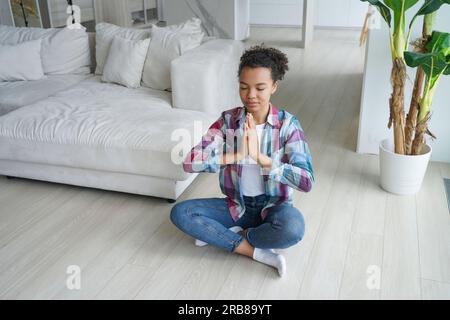 Ruhiges birassisches Mädchen praktiziert Yoga in Lotus Pose zu Hause, fördert einen gesunden Lebensstil und Stresslinderung. Stockfoto