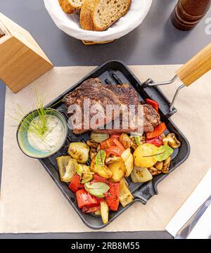 Gegrillte Schweinekoteletts mit geröstetem Gemüse, serviert mit Sauce in der Eisentasse, Restaurantmenü, Draufsicht Stockfoto