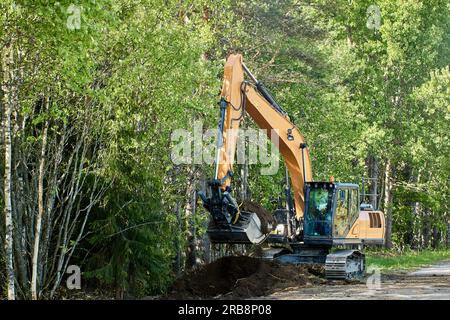 Straßenarbeiten, Raupenbagger vertieft den Abfluss am Straßenrand auf dem Land, Reparatur des Entwässerungssystems. Stockfoto