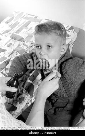 Ein Junge ist krank und nimmt seine Medizin nicht. Seine Mutter hält einen Löffel und wartet darauf, dass er ihn nimmt, und das tut er. Er öffnet seinen Mund und nimmt ihn, obwohl er nicht so gut schmeckt. Schweden 1956. Conard Ref. 3157. Stockfoto