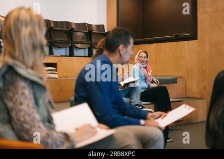 Multikulturelle Menschen, die eine Präsentation bei der Arbeit halten. Muslimische rothaarige Mitarbeiterin, die ihren Kollegen während der Präsentation bei der Arbeit zuhört Stockfoto