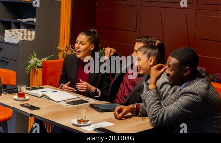 Eine Gruppe von multirassischen Geschäftsleuten spricht und lächelt, während sie im Café sitzen Stockfoto
