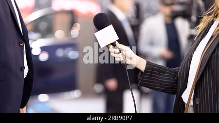 Ein Fernsehjournalist, der das Mikrofon hält, macht ein Presseinterview mit einem unbekannten männlichen Geschäftsmann Stockfoto