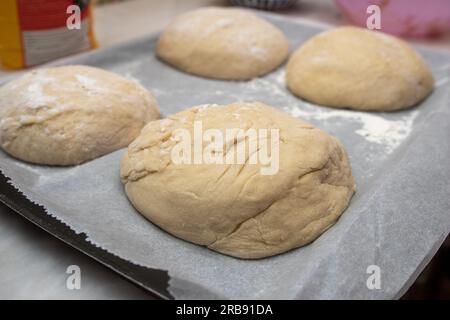 Der Prozess des Backens zu Hause. Nahaufnahme von süßem Brotteig in Form von Brötchen auf einem Tablett, bevor er in den Ofen geht Stockfoto