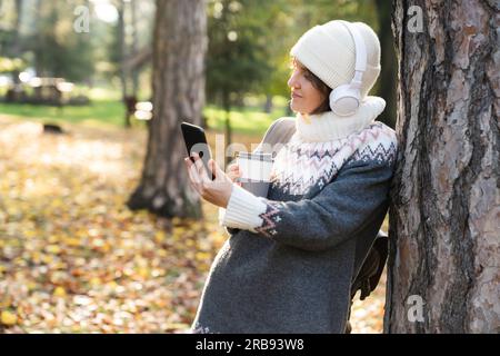 Eine Frau hält ein Telefon und eine Tasse heißes Getränk in der Hand. Frau macht Selfie auf Smartphone Stockfoto