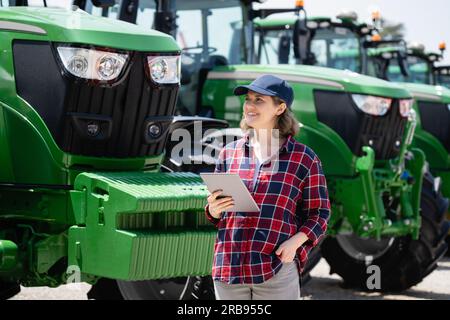 Landwirtin mit einem digitalen Tablet auf dem Hintergrund eines landwirtschaftlichen Traktors Stockfoto
