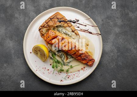 Ein Stück gegrilltes Lachsfilet mit Ciabatta und Sauce auf einem leichten Teller Stockfoto