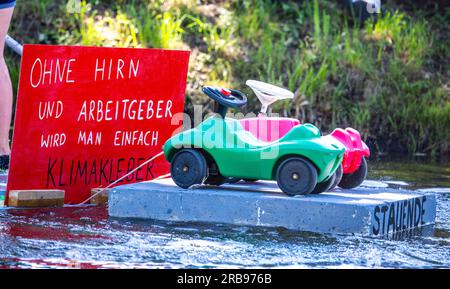 Pokrent, Deutschland. 08. Juli 2023. Das Team „Allerletzte Generation“ beginnt bei der traditionellen Badewannen-Regatta auf dem Dorfteich. Ein Schild mit dem Slogan „ohne Gehirn und Arbeitgeber werden Sie zum Klimakleber“ ist zu sehen. Insgesamt zehn Boote starten in zwei Rennen auf der Teichstrecke. Neben der Geschwindigkeit wird auch die Originalität der Boote vom Publikum bewertet. Kredit: Jens Büttner/dpa/Alamy Live News Stockfoto