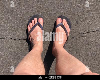 Füße in Gummisandalen, die auf Gras und Schmutzboden treten. Chinelo Havaianas Stockfoto