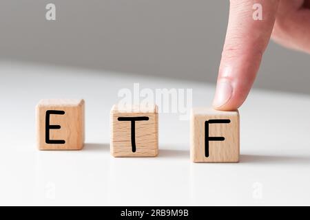 Text ETF auf Holzwürfeln auf weißem, strukturiertem Kitthintergrund. Abkürzung für „börsengehandelte Fonds“. Quadratische Holzblöcke. Draufsicht, flach liegend. Stockfoto