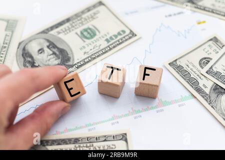 Holzwürfel mit blauen Buchstaben, die das Wort ETFS (Exchange Traded Funds) auf Dollarscheinen auf einem Tisch bilden. Foto des Investitionskonzepts. Stockfoto