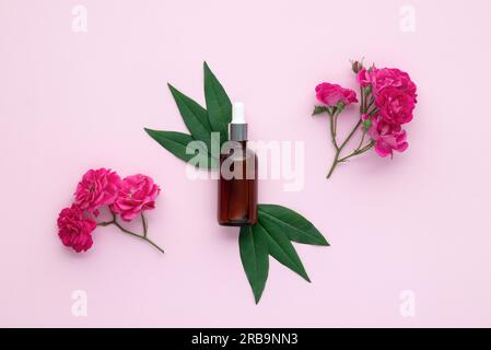 Flasche mit ätherischem Rosenöl für Gesichtsmassage. Glasfläschchen und grüne Blätter auf pinkfarbenem Papierhintergrund, Draufsicht. Blumenduft. Flach liegend, Komposition wi Stockfoto