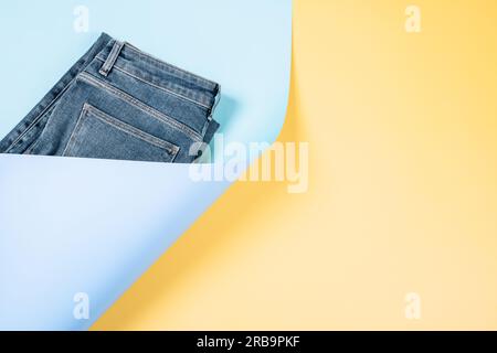 Trendige Komposition mit einem Teil neuer Jeans auf hellblauem und pastellgelbem Hintergrund. Abstrakter Denim-Hintergrund. Jeansladen, Einkaufen, Verkauf, Recycling Stockfoto