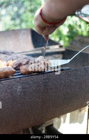 Mititei. Drehen Sie die Mititei mit einer Gabel auf den Grill. Mititei oder Mici, typische rumänische und moldauische Speisen, gegrillte Hackfleischrollen aus einer Mischung Stockfoto