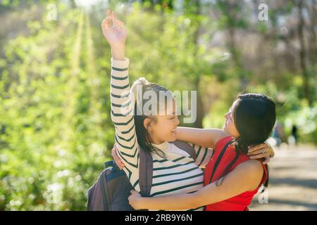 Fröhliche asiatische Frauen, die sich während ihrer gemeinsamen Reise im Wald umarmen Stockfoto