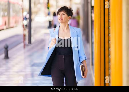 Eine stilvolle Frau in eleganten, formellen Kleidern, die auf der Straße spazieren geht Stockfoto