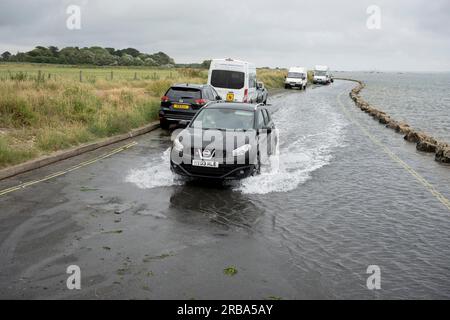 Am 4. Juli 2023 in Milford-on-Sea, Hampshire, England, spritzt ein Auto durch aufsteigendes Meerwasser auf der Saltgrass Lane mit Blick auf den Solent. Stockfoto