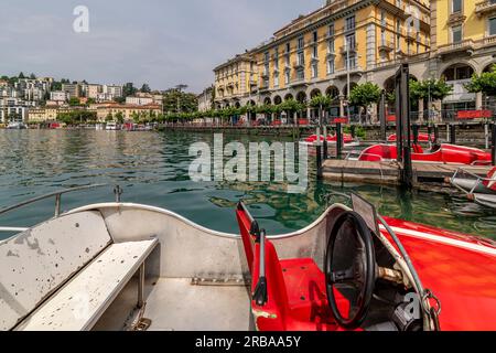 Lustige rote Rennboote auf dem Luganer See, Schweiz, mit der Stadt im Hintergrund Stockfoto