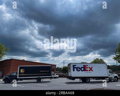 Suwanee, GA/USA - 17. Mai 2023: Ein UPS- und FedEx-Lkw stehen am 30. Mai 2023 gegenüber auf einem Parkplatz mit Sturmwolken. Stockfoto