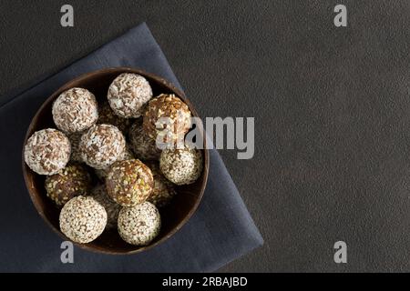 Vegetarische Süßigkeiten-Energiebälle mit Nüssen, getrocknete Früchte in der Holzschüssel auf Serviettenplatte lagen auf dunklem Hintergrund mit Kopierbereich. Hausgemachtes Bio-Essen Stockfoto