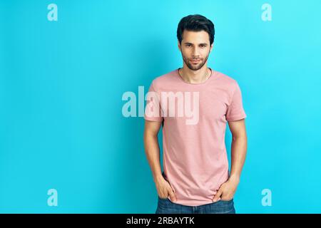 Junger schöner Mann Porträt trägt rosa T-Shirt Blick auf die Kamera Auf blauem Hintergrund mit Kopierplatz Stockfoto