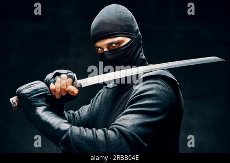 Kampf Ninja posiert mit einem Schwert über schwarzem Hintergrund. japanische Kämpfer Konzept Stockfoto