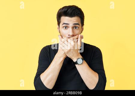 Schockierter Mann, der den Mund mit Händen über gelbem Hintergrund bedeckt. Emotionen und geheimes Konzept Stockfoto