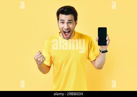 Aufgeregt schreienden Mann hält Handy und Blick auf die Kamera in gelben Studio Hintergrund. Kommunikationskonzept Stockfoto