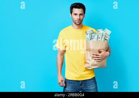 Handsome Mann halten Papiertüte voller Stapel von Geld isoliert auf blauem Hintergrund. Erfolg, Geschäft und Vermögen Konzept Stockfoto