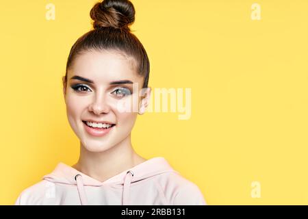 Headshot Porträt der jungen glücklichen Frau lächelt und schaut auf die Kamera mit Kopieplatz über gelben Hintergrund. Nahaufnahme weibliche Schönheit Gesicht Stockfoto