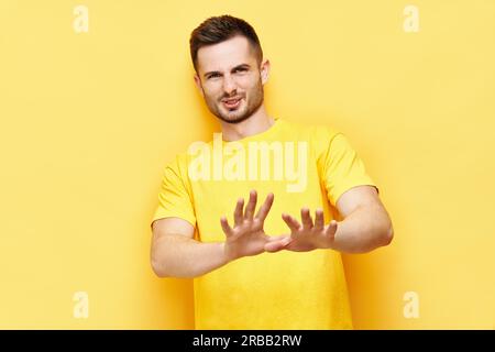Junger unzufriedener Mann macht Stop-Geste Schild sagen, keine isoliert auf gelbem Hintergrund. Negative Emotionen, Gesichtsausdruck Stockfoto