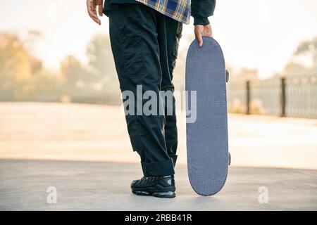 Zugeschnittenes Bild eines Skaters, der Skateboard auf der Straße hält. Extremsportkonzept Stockfoto