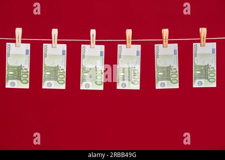 Geldwäsche, Euro-Banknoten hängen am Seil über rotem Studiohintergrund. Konzept für Finanzen, Korruption, kriminelle Aktivitäten Stockfoto