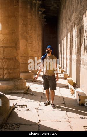 Junger Mann in blauem Turban, der auf den Säulen des Edfu Tempels in der Nähe der Stadt Assuan spaziert. Ägypten, Westufer des nils in der Stadt Edfu Stockfoto