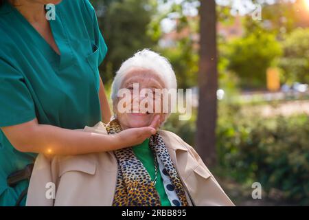 Eine ältere Frau mit der Krankenschwester auf einem Spaziergang im Garten eines Pflegeheims im Rollstuhl neben der Natur Stockfoto