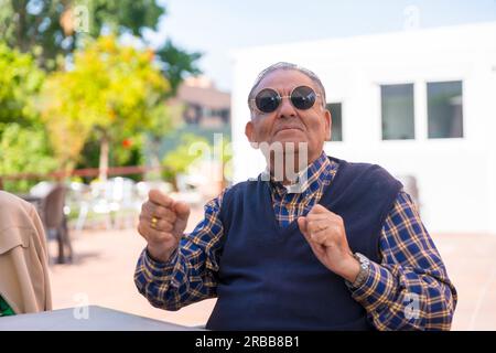 Ein älterer Mann tanzt im Garten eines Pflegeheims oder Seniorenheims auf einer Sommerparty mit Sonnenbrille Stockfoto